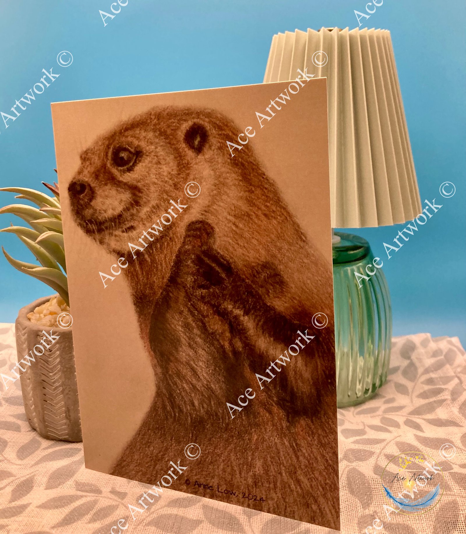 Otter greeting card displayed upright in a styled setting beside a decorative lamp and small plant