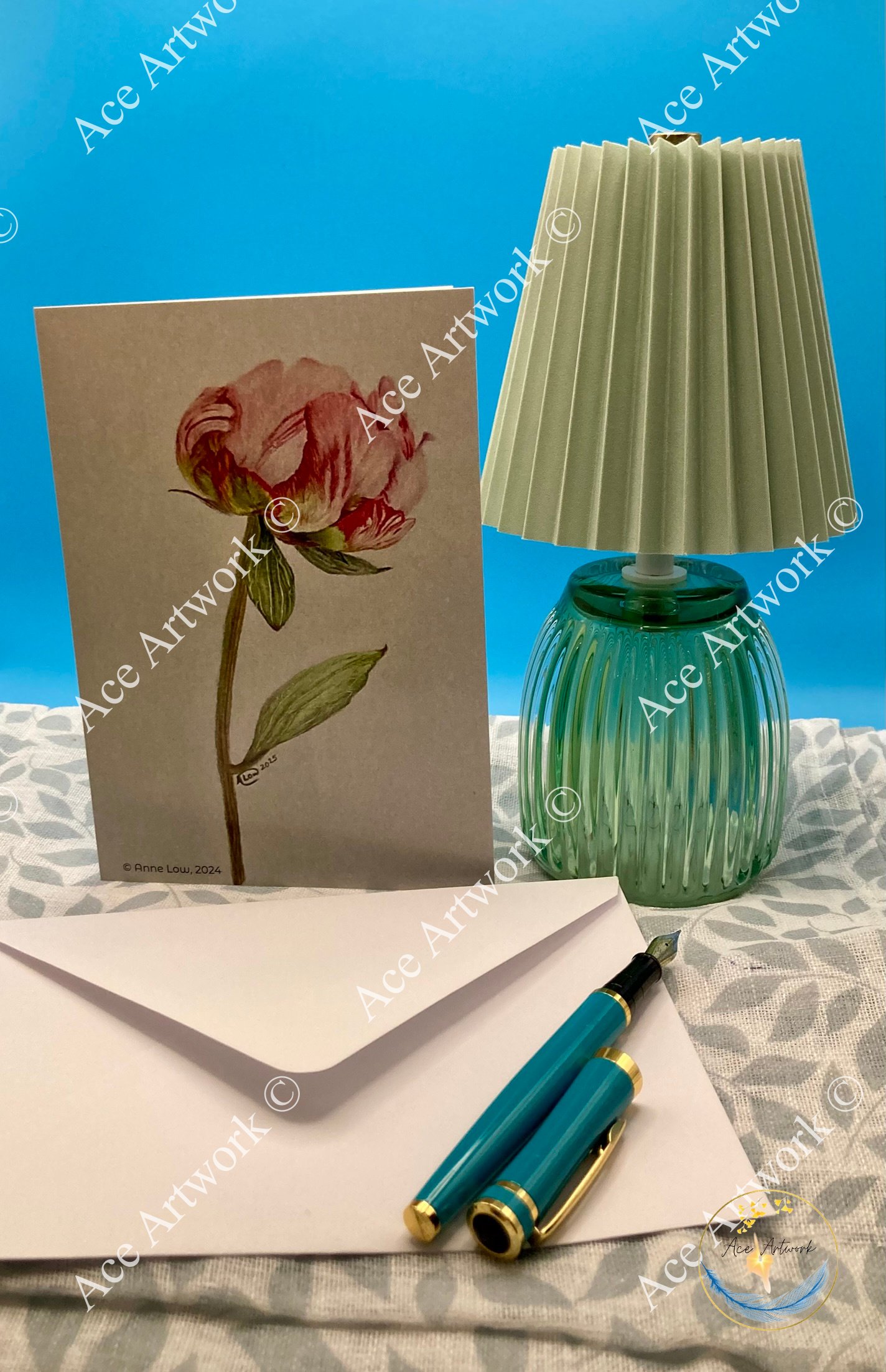 Peony greeting card displayed upright in a styled setting beside a decorative lamp, open envelope and a fountain pen